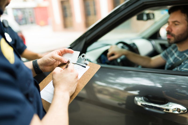 policeman writing ticket to man in car